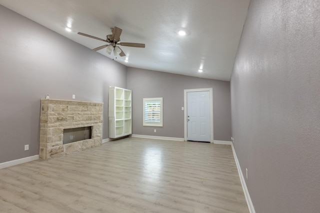 unfurnished living room with vaulted ceiling, a stone fireplace, wood finished floors, and baseboards