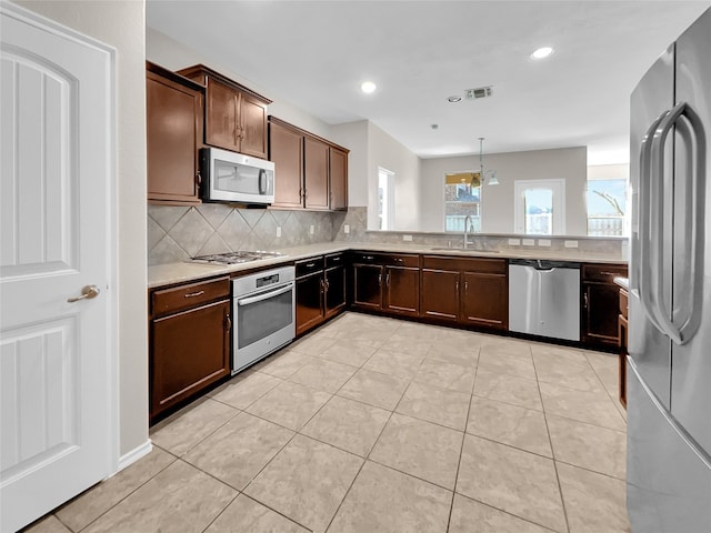 kitchen with tasteful backsplash, stainless steel appliances, light tile floors, decorative light fixtures, and sink