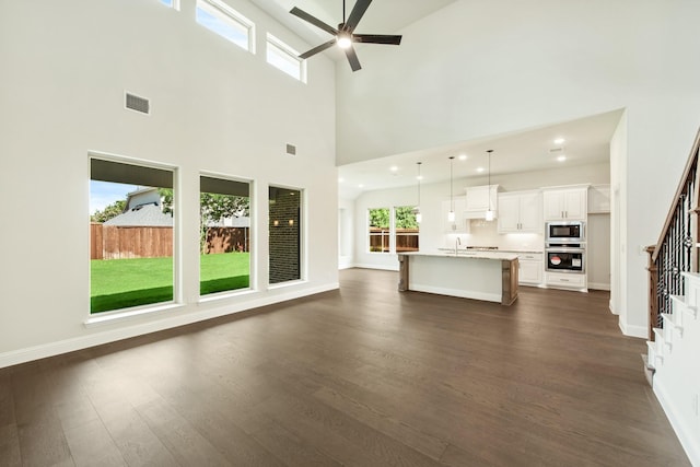 unfurnished living room with baseboards, visible vents, ceiling fan, dark wood-style flooring, and stairs