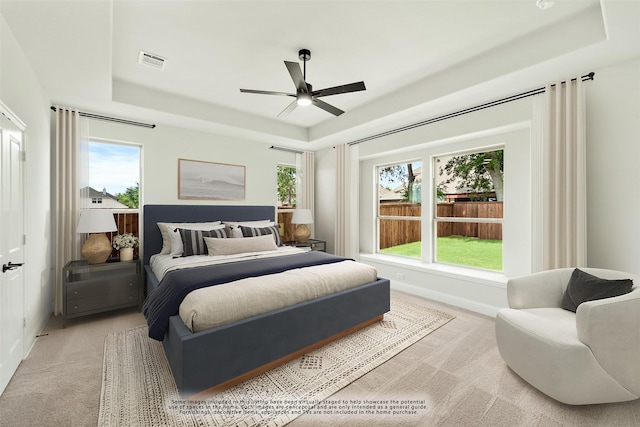 bedroom with multiple windows, a raised ceiling, and light colored carpet