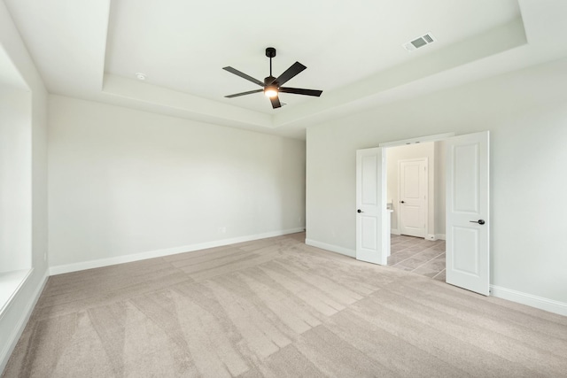 unfurnished room with a raised ceiling, light carpet, visible vents, and baseboards