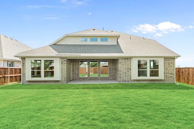 rear view of property with a yard, a shingled roof, a fenced backyard, and brick siding