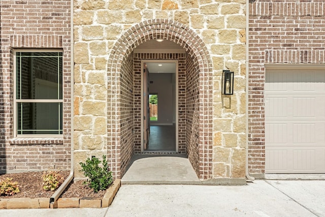 entrance to property featuring an attached garage and brick siding