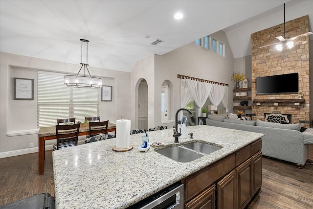 kitchen with sink, light stone counters, dark hardwood / wood-style floors, an island with sink, and lofted ceiling