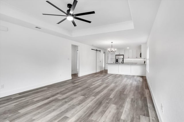 unfurnished living room featuring light hardwood / wood-style floors, a tray ceiling, and ceiling fan with notable chandelier