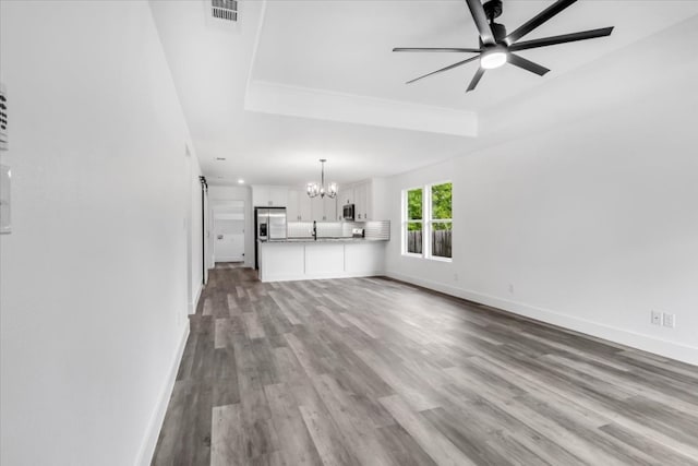 unfurnished living room with dark hardwood / wood-style flooring, sink, a raised ceiling, and ceiling fan with notable chandelier