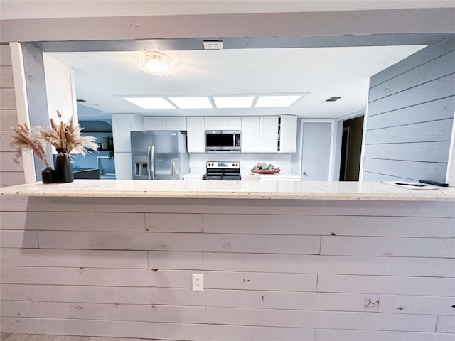 kitchen featuring appliances with stainless steel finishes, light stone counters, and white cabinetry