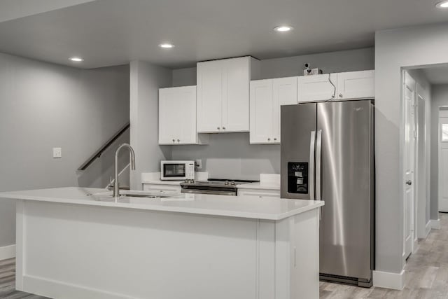 kitchen featuring appliances with stainless steel finishes, sink, white cabinetry, a kitchen island with sink, and light wood-type flooring