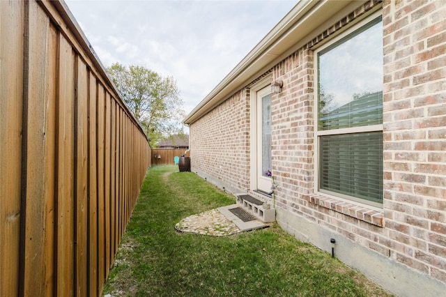 view of property exterior with a yard, fence, and brick siding