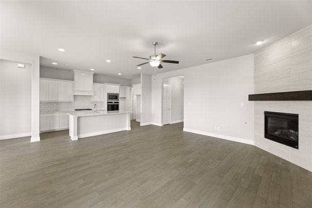 unfurnished living room with dark wood-type flooring, ceiling fan, a fireplace, and sink