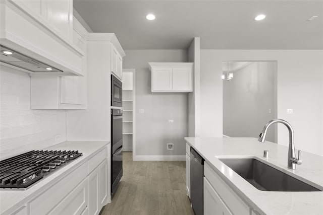 kitchen with premium range hood, sink, stainless steel appliances, light stone countertops, and white cabinets