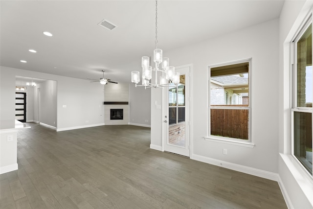 unfurnished dining area with ceiling fan with notable chandelier, a fireplace, and dark hardwood / wood-style floors