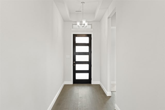 doorway to outside featuring a raised ceiling, dark hardwood / wood-style floors, and an inviting chandelier