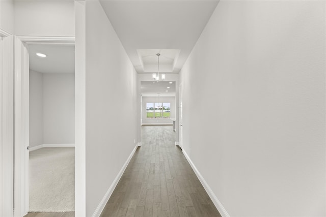 hall featuring a chandelier, hardwood / wood-style floors, and a raised ceiling