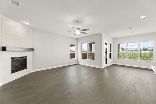 unfurnished living room with a fireplace, dark hardwood / wood-style flooring, ceiling fan with notable chandelier, and a wealth of natural light