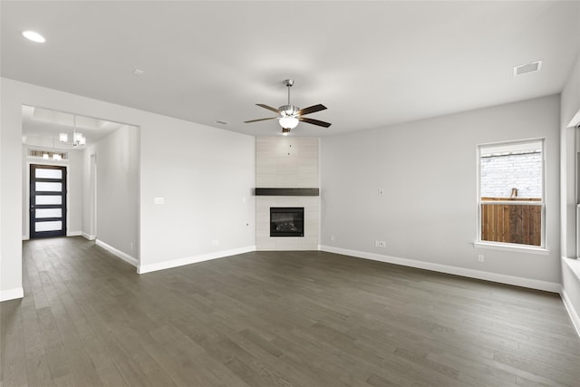 unfurnished living room featuring a tile fireplace, dark wood-type flooring, and ceiling fan with notable chandelier