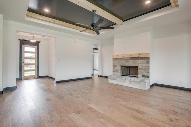 unfurnished living room featuring light wood-type flooring, baseboards, a tray ceiling, and a stone fireplace