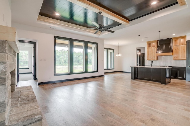 kitchen with decorative backsplash, an island with sink, custom range hood, open floor plan, and pendant lighting