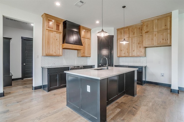 kitchen with custom range hood, visible vents, glass insert cabinets, a kitchen island with sink, and a sink