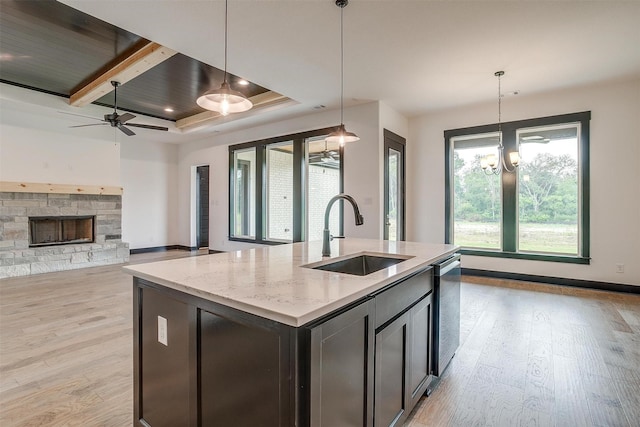 kitchen with hanging light fixtures, a center island with sink, light stone counters, and a sink