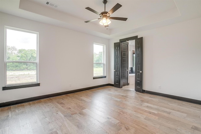 empty room featuring visible vents, a tray ceiling, light wood-style flooring, and baseboards