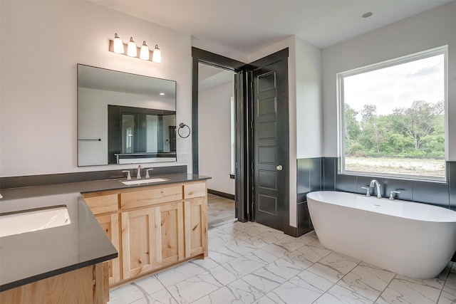 full bath featuring marble finish floor, a freestanding tub, and vanity