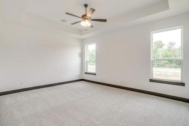 unfurnished room featuring carpet floors, a tray ceiling, baseboards, and a ceiling fan