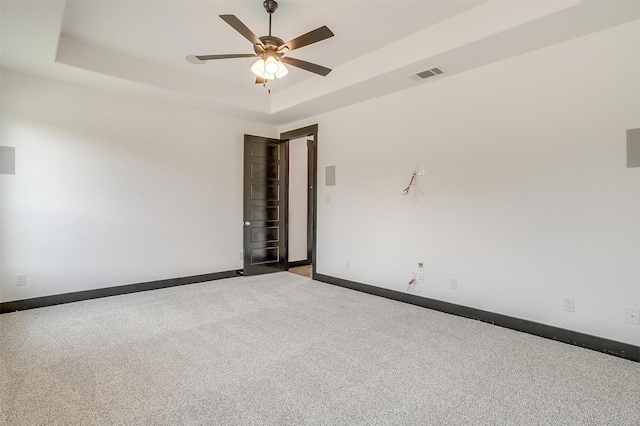 empty room with light carpet, a ceiling fan, visible vents, baseboards, and a raised ceiling