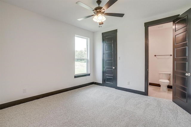 unfurnished bedroom with light tile patterned floors, light colored carpet, ensuite bathroom, a ceiling fan, and baseboards