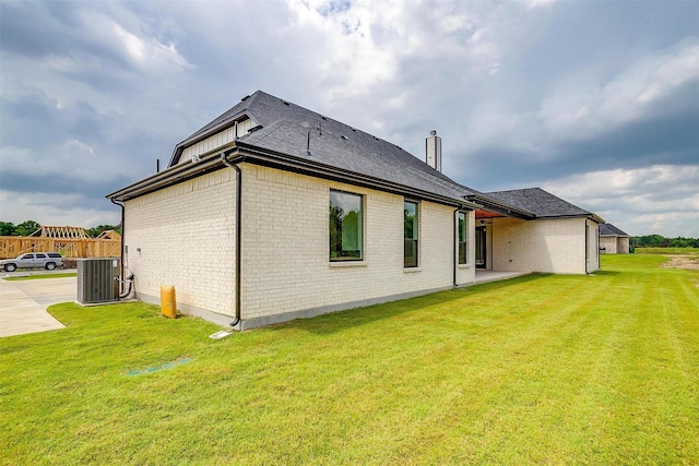 rear view of house featuring central air condition unit, brick siding, and a yard