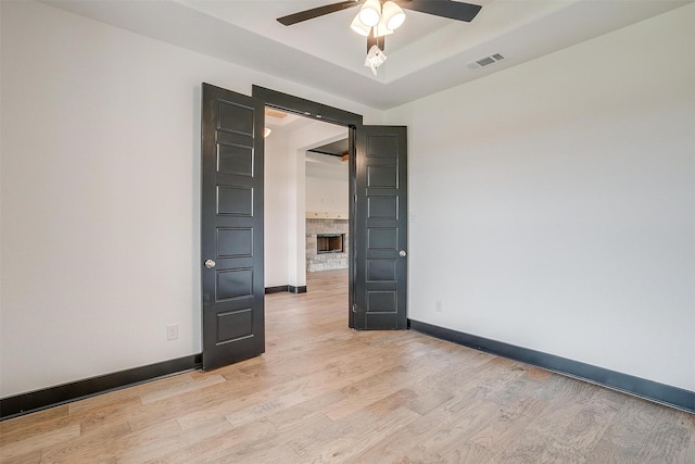 empty room featuring a tray ceiling, visible vents, light wood-style floors, a ceiling fan, and baseboards