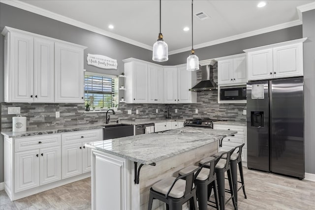 kitchen with wall chimney exhaust hood, appliances with stainless steel finishes, a kitchen island, light stone counters, and white cabinetry