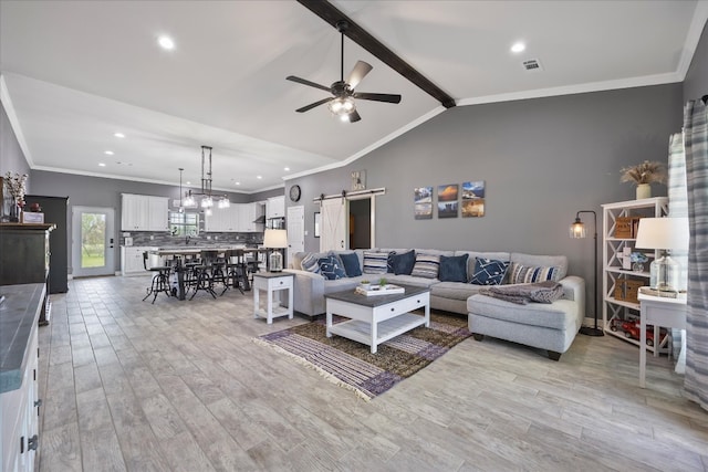 living room featuring lofted ceiling with beams, crown molding, ceiling fan, a barn door, and light wood-type flooring