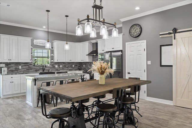 kitchen with light stone counters, wall chimney exhaust hood, a barn door, stainless steel refrigerator, and hanging light fixtures