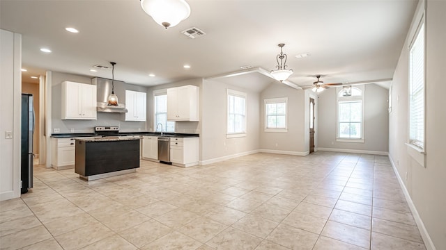 kitchen featuring appliances with stainless steel finishes, a kitchen island, white cabinets, hanging light fixtures, and wall chimney exhaust hood