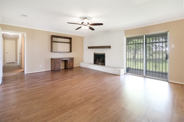 unfurnished living room featuring ceiling fan, hardwood / wood-style floors, a fireplace, ornamental molding, and a textured ceiling