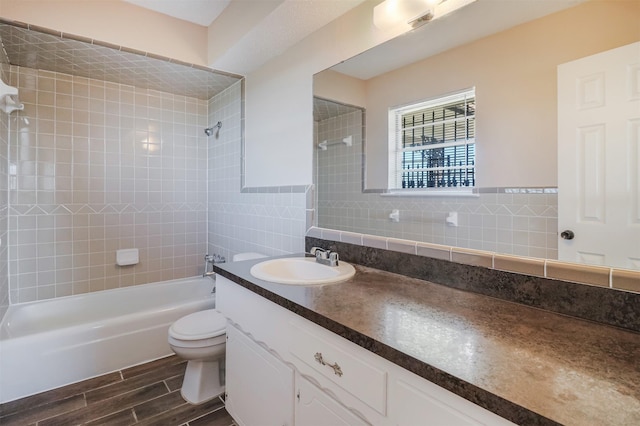 full bathroom with tile walls, tiled shower / bath, vanity, and toilet