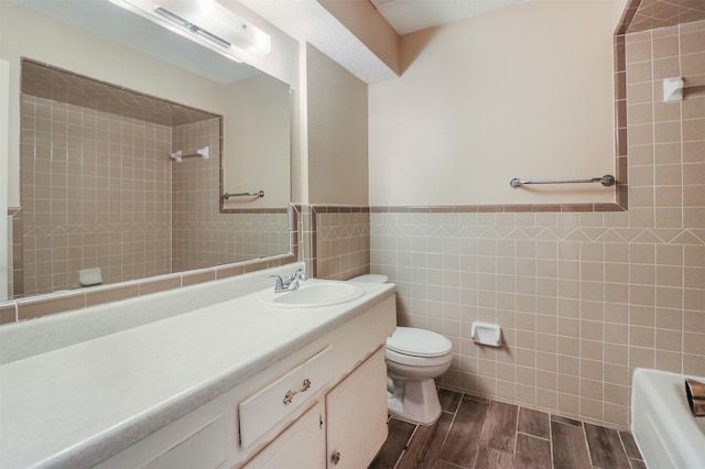 bathroom with tile walls, vanity, toilet, and a tile shower