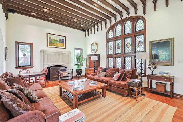 living room featuring light wood-style flooring, a fireplace with flush hearth, beam ceiling, and a high ceiling