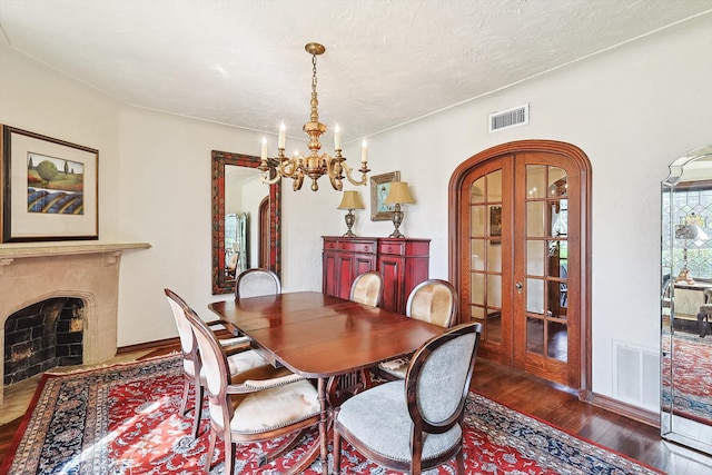 dining space with dark wood-type flooring, an inviting chandelier, and french doors