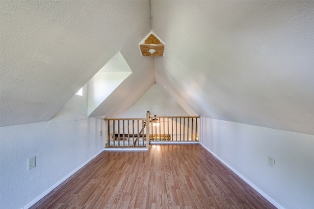 additional living space with a textured ceiling, hardwood / wood-style flooring, and vaulted ceiling