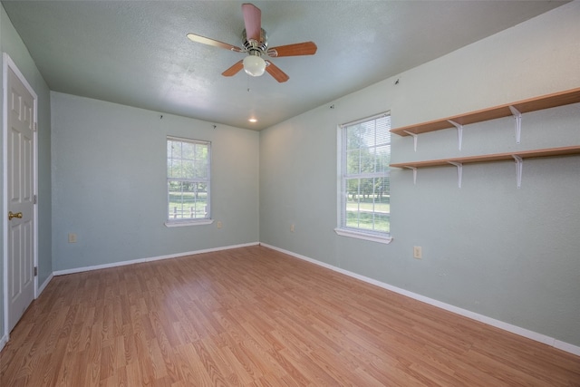 empty room with a healthy amount of sunlight, ceiling fan, light hardwood / wood-style floors, and a textured ceiling