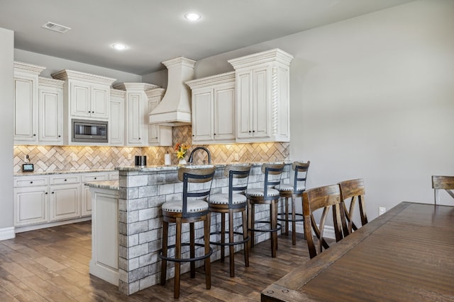 kitchen featuring dark hardwood / wood-style flooring, custom exhaust hood, a breakfast bar area, and stainless steel microwave