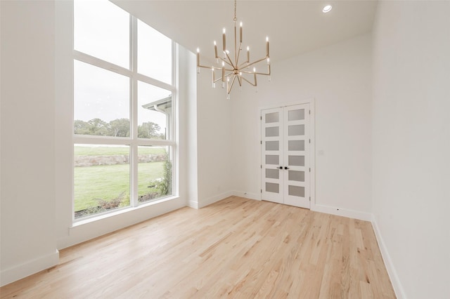 unfurnished dining area with light wood-type flooring, a towering ceiling, and an inviting chandelier