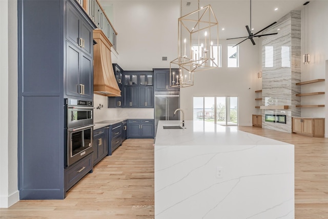 kitchen with blue cabinets, sink, hanging light fixtures, appliances with stainless steel finishes, and light stone counters