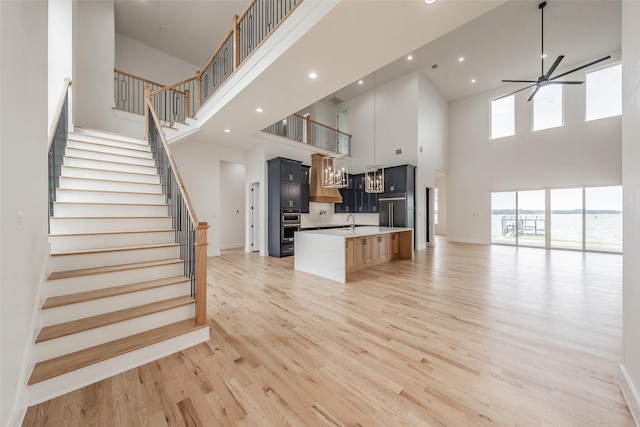 kitchen with ceiling fan, a center island with sink, light hardwood / wood-style floors, and a high ceiling