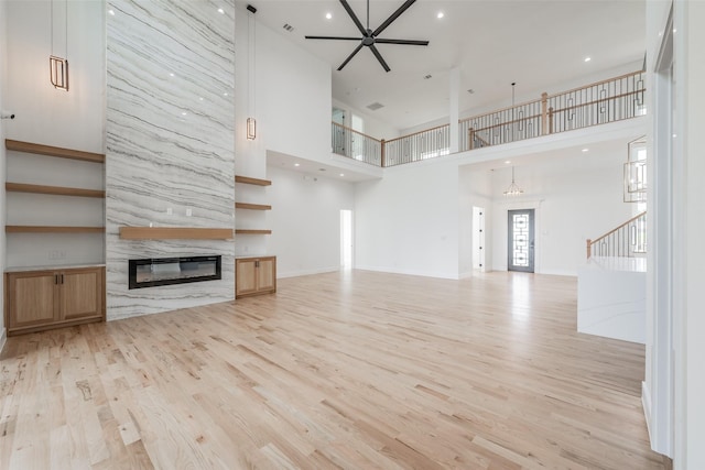 unfurnished living room featuring ceiling fan, light wood-type flooring, a towering ceiling, and a high end fireplace