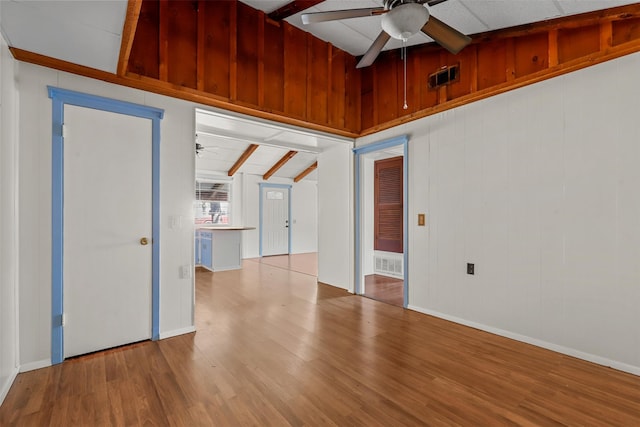 empty room featuring beamed ceiling, ceiling fan, light hardwood / wood-style floors, and wood walls