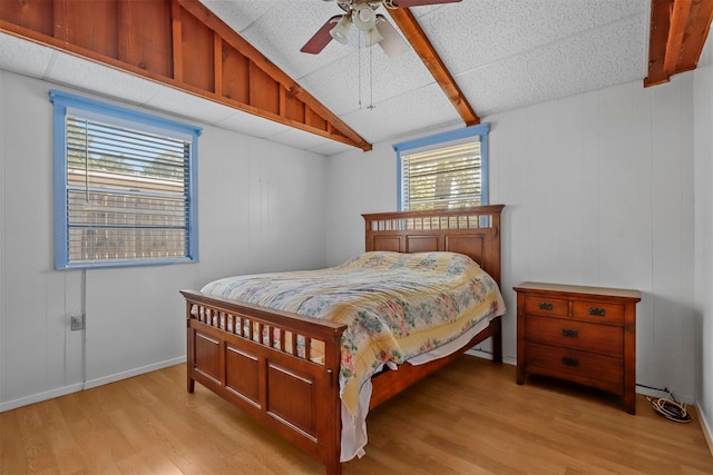 bedroom featuring ceiling fan, lofted ceiling, light wood-type flooring, and wooden walls