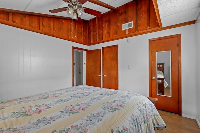 bedroom with wooden walls, light hardwood / wood-style flooring, a paneled ceiling, and ceiling fan